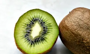 Czy pies może jeść kiwi? Na zdjęciu przekrojone kiwi z widocznymi czarnymi pestkami i całe, owłosione kiwi obok.