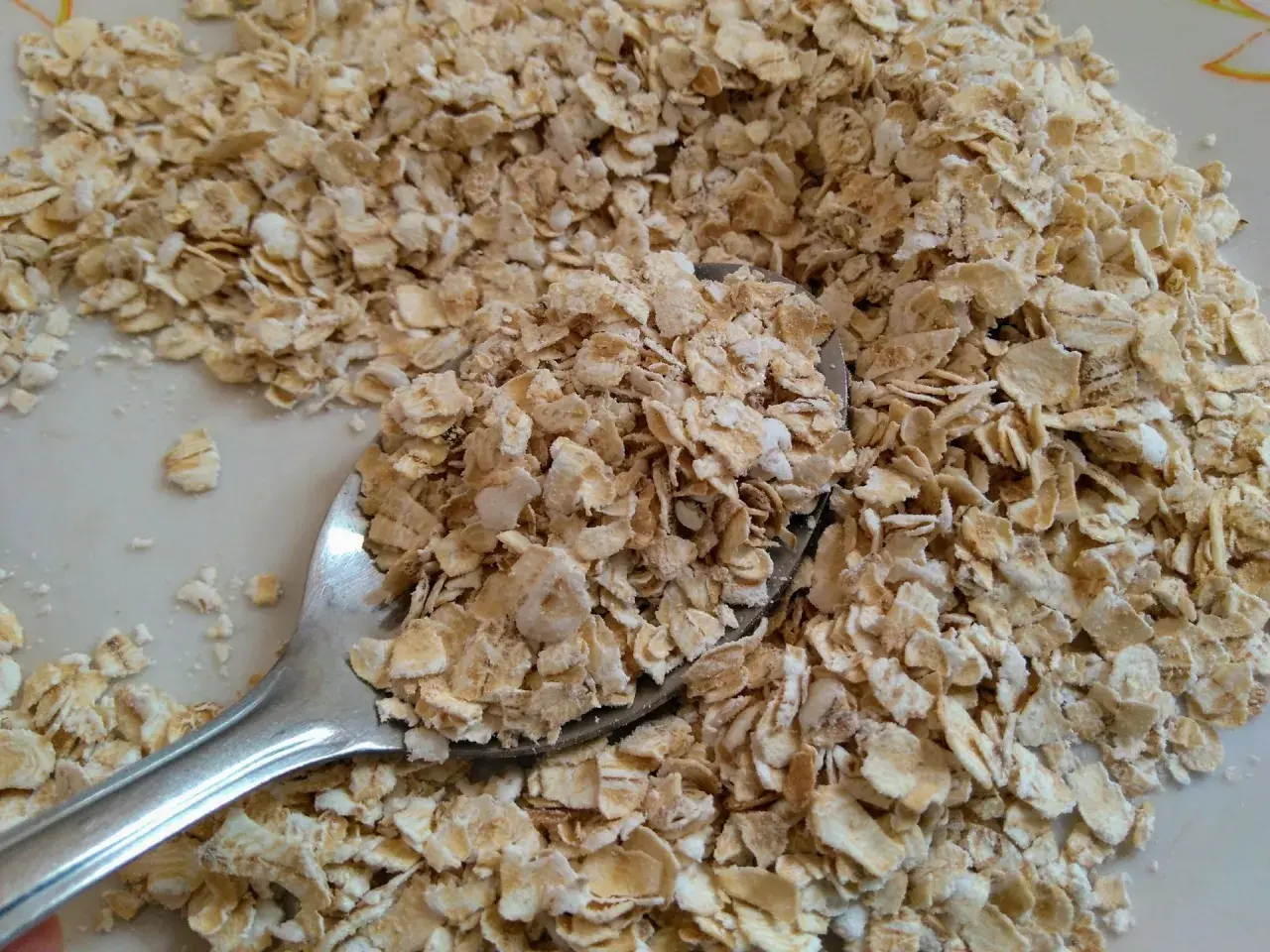Łyżka płatków owsianych na talerzu. Czy pies może jeść płatki owsiane? Tak, w umiarkowanych ilościach, jako dodatek do diety.